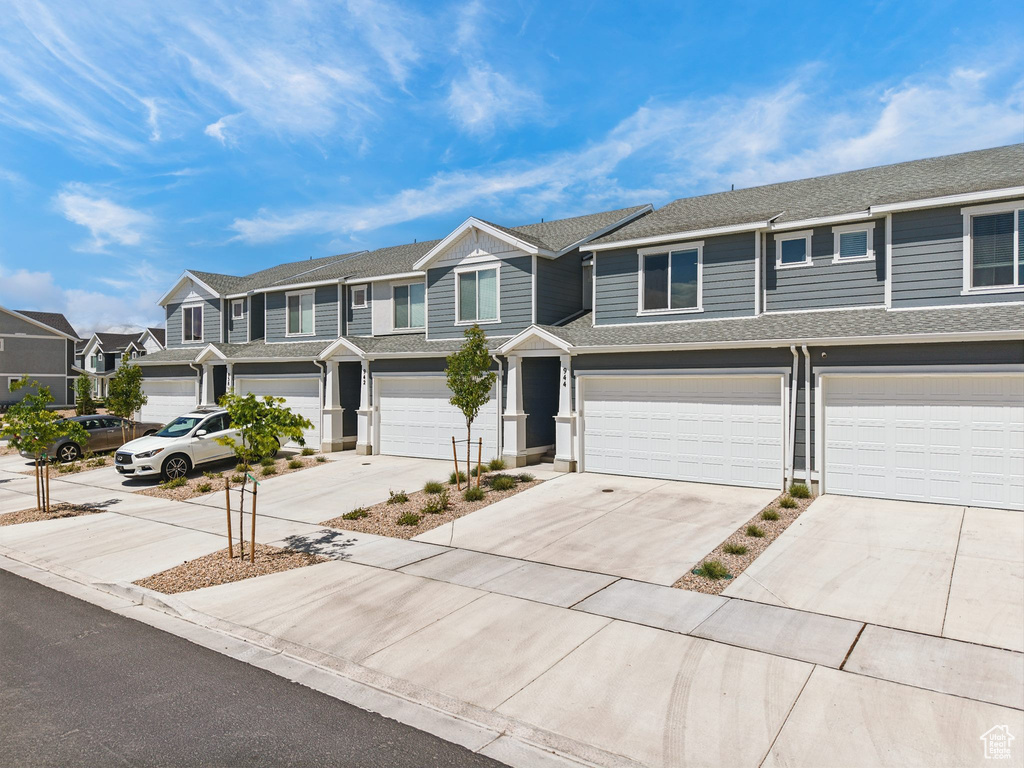 View of property featuring a residential view, driveway, an attached garage, and a shingled roof