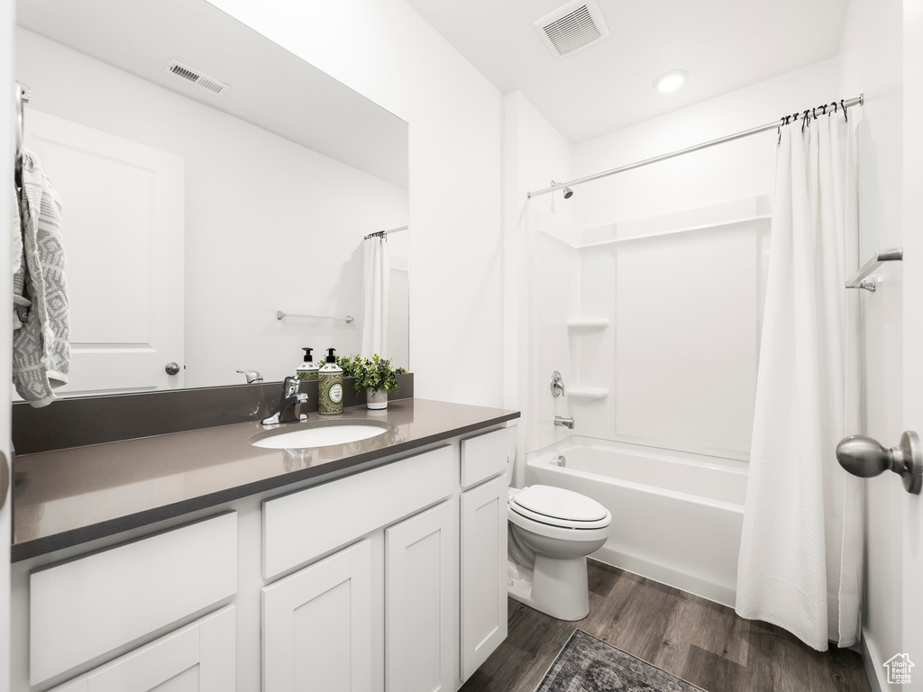 Bathroom featuring wood finished floors, toilet, vanity, and shower / tub combo