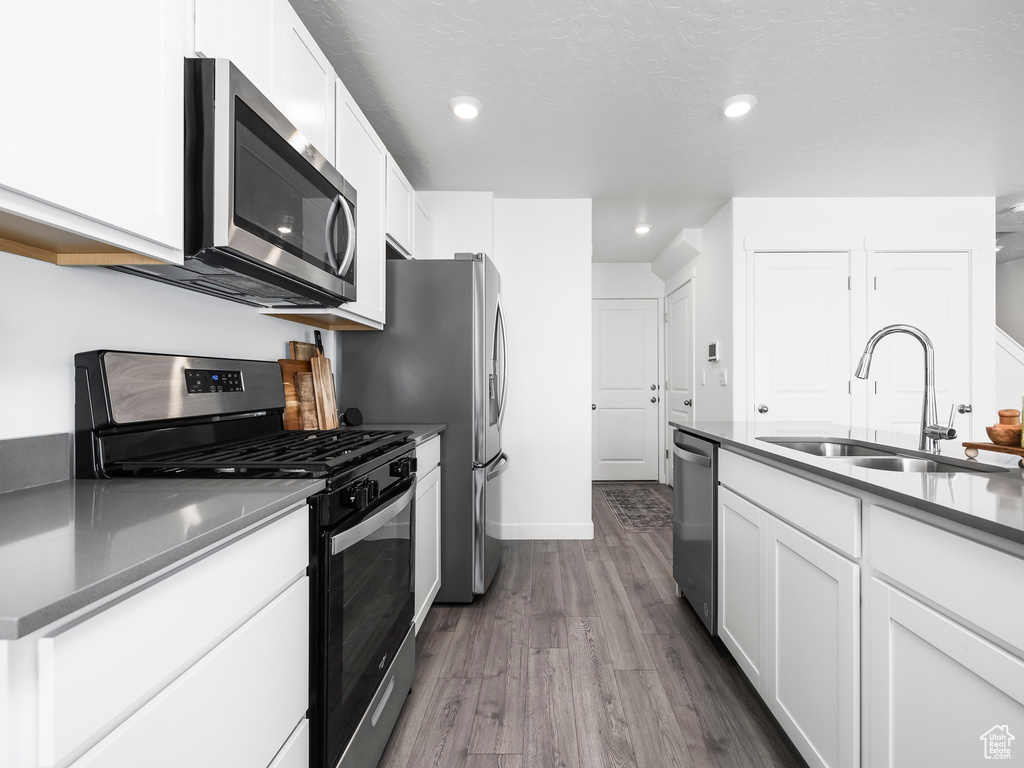 Kitchen with appliances with stainless steel finishes, a sink, dark wood finished floors, white cabinets, and recessed lighting