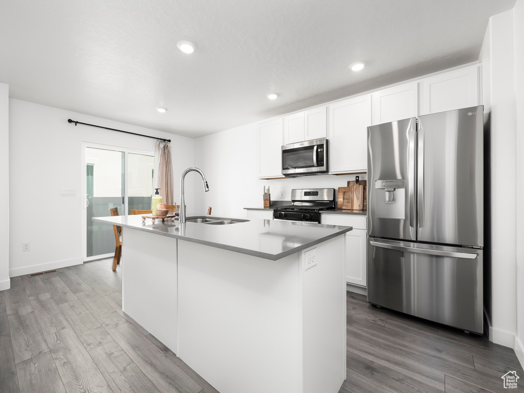 Kitchen featuring appliances with stainless steel finishes, a sink, wood finished floors, white cabinetry, and recessed lighting