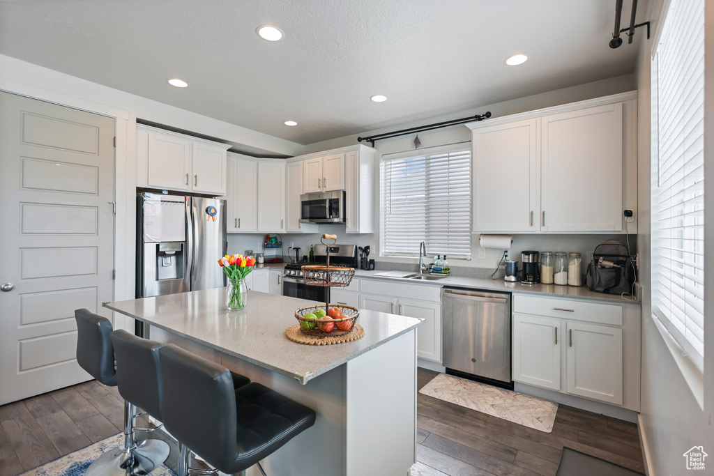 Kitchen featuring appliances with stainless steel finishes, white cabinetry, dark wood-type flooring, a kitchen bar, and recessed lighting