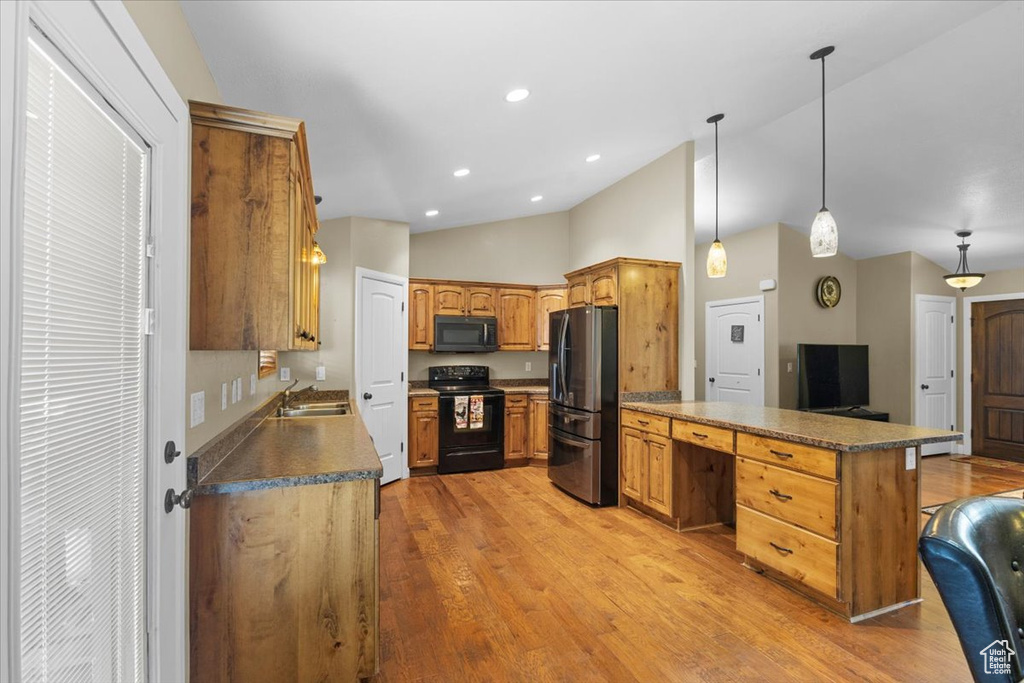 Kitchen featuring a peninsula, a sink, black appliances, light wood-style floors, and vaulted ceiling