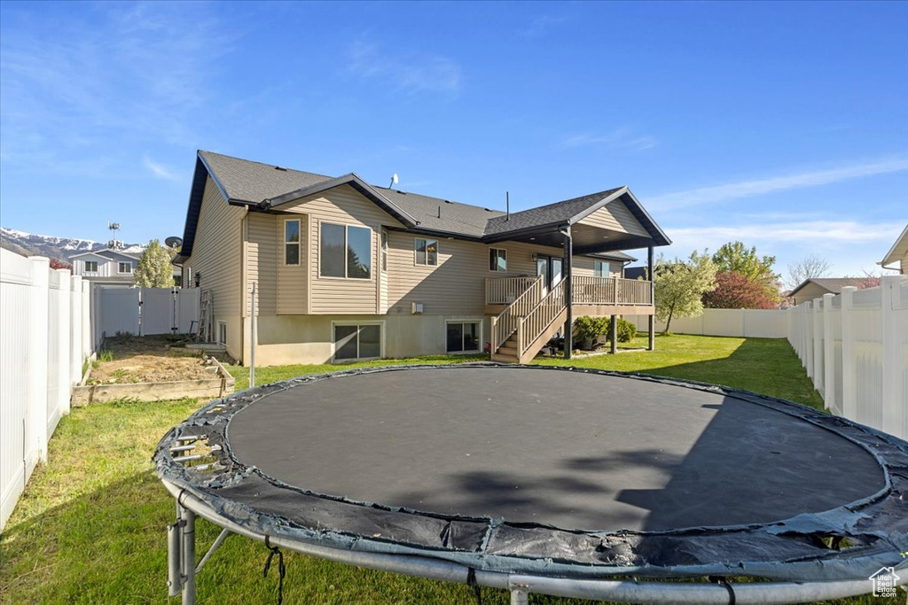 Rear view of house with a trampoline, a yard, stairway, and a fenced backyard