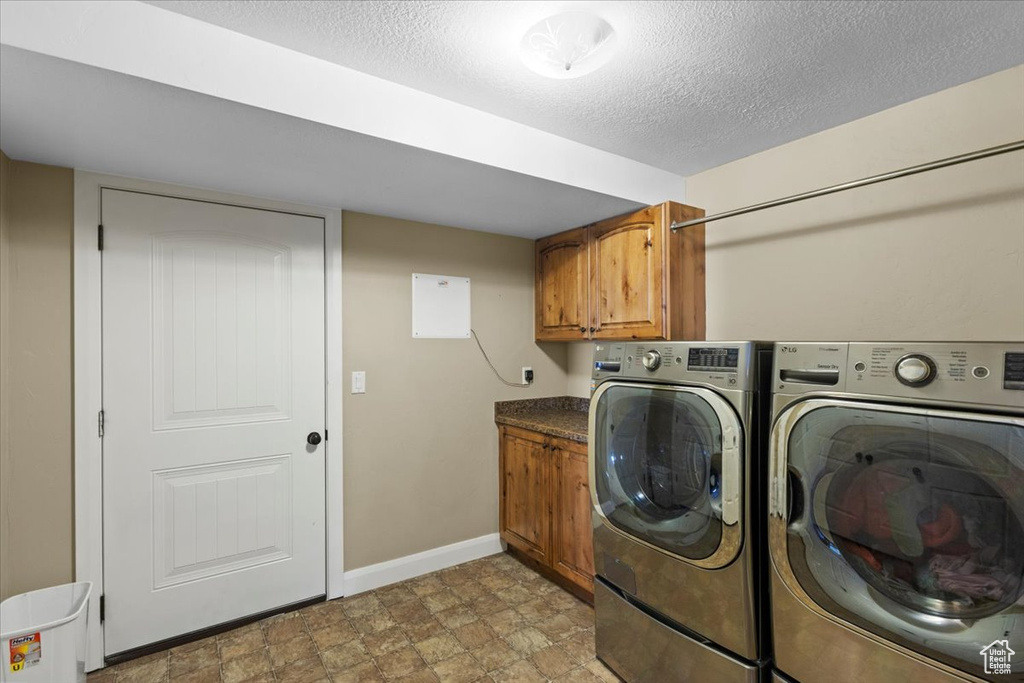 Laundry area featuring washing machine and dryer, cabinet space, baseboards, a textured ceiling, and stone finish flooring
