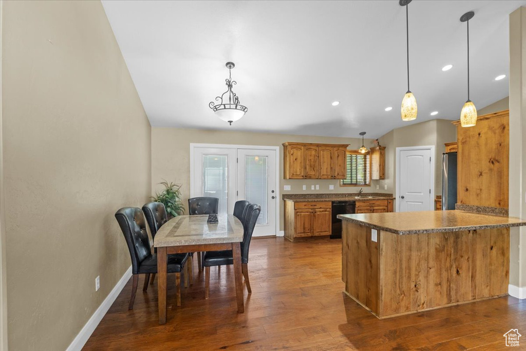 Kitchen featuring a peninsula, black dishwasher, freestanding refrigerator, decorative light fixtures, and dark wood finished floors
