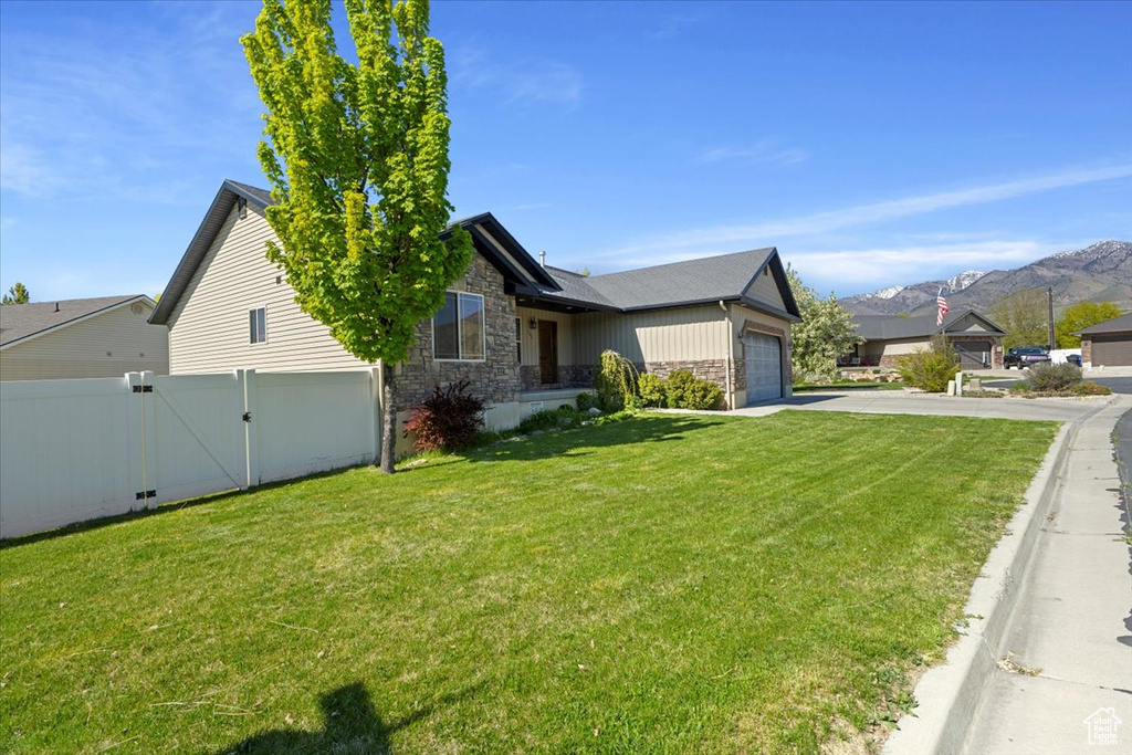 View of front facade featuring an attached garage, a front lawn, stone siding, and driveway