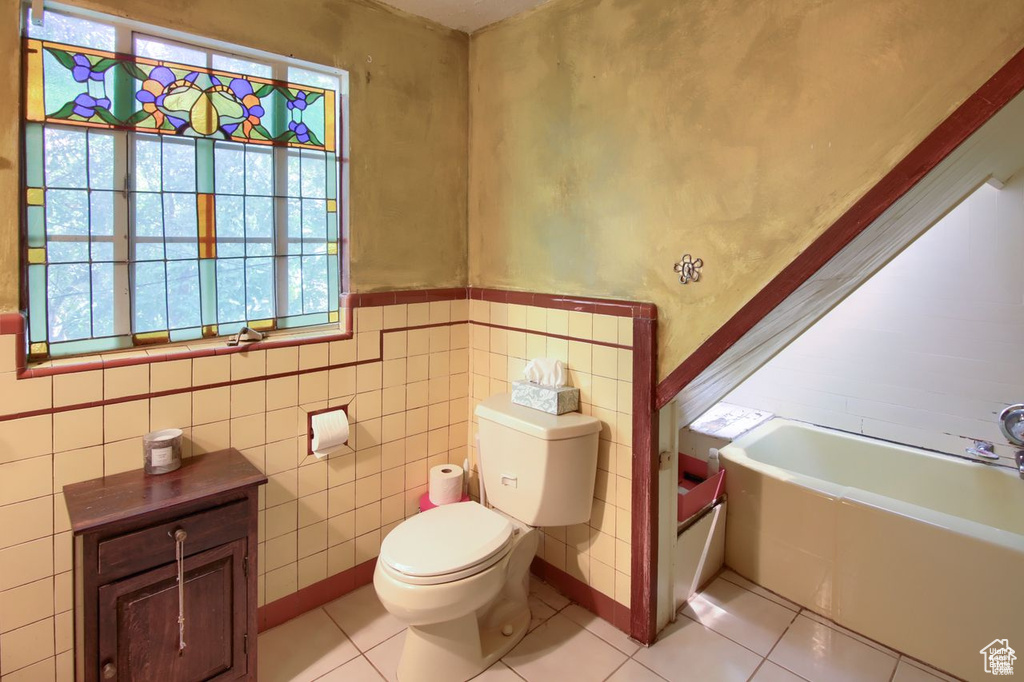 Bathroom featuring tile patterned floors, toilet, a tub to relax in, tile walls, and a wainscoted wall