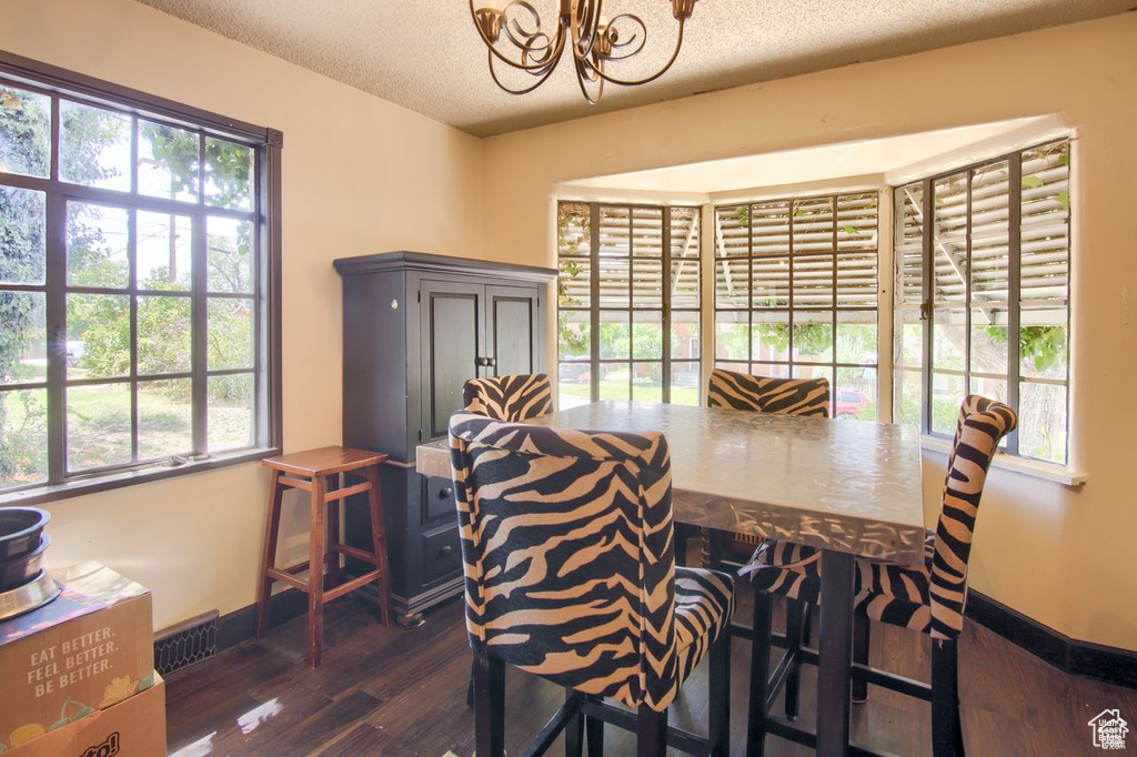 Dining area featuring wood finished floors, a chandelier, a textured ceiling, and baseboards