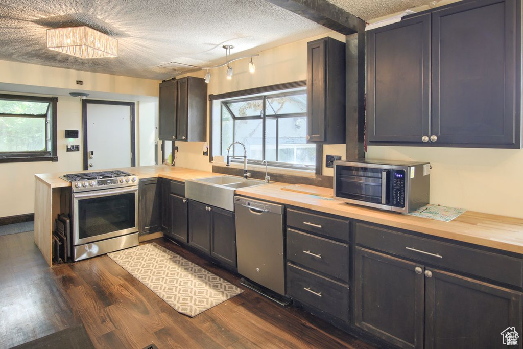 Kitchen with stainless steel appliances, a sink, dark wood finished floors, a peninsula, and wood counters