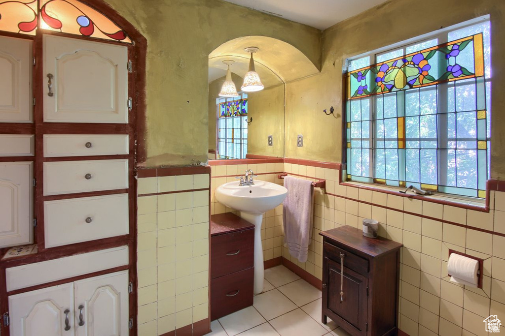 Bathroom with tile patterned flooring, tile walls, healthy amount of natural light, a wainscoted wall, and a sink