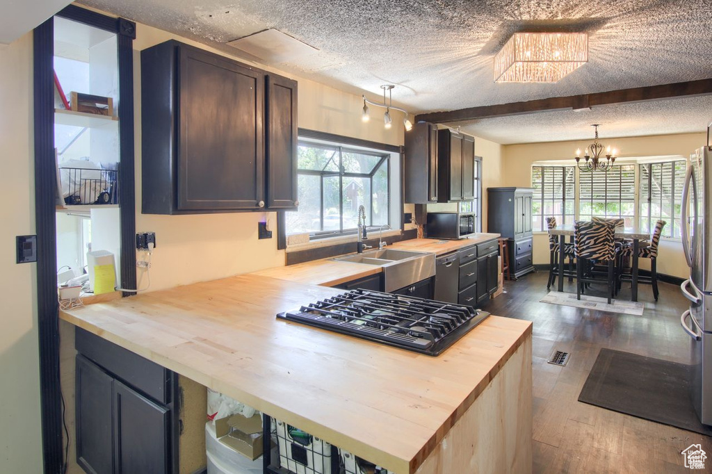 Kitchen featuring butcher block countertops, stainless steel appliances, a sink, a textured ceiling, and dark wood-type flooring
