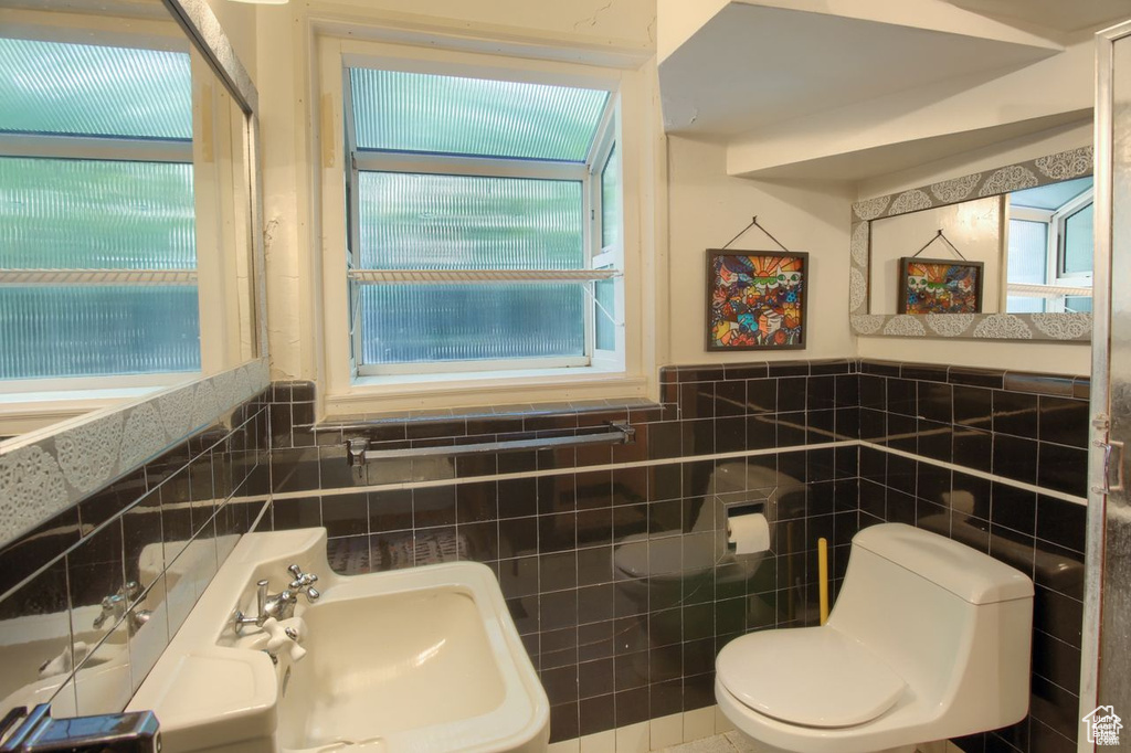 Half bath featuring tile walls, toilet, plenty of natural light, a wainscoted wall, and a sink