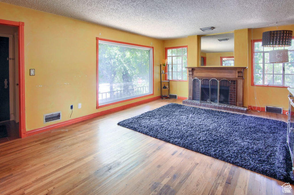 Living room with wood finished floors, a textured ceiling, healthy amount of natural light, a fireplace, and baseboards
