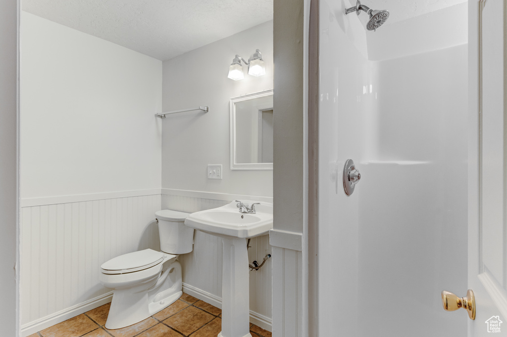 Bathroom with toilet, tile patterned flooring, wainscoting, and a shower