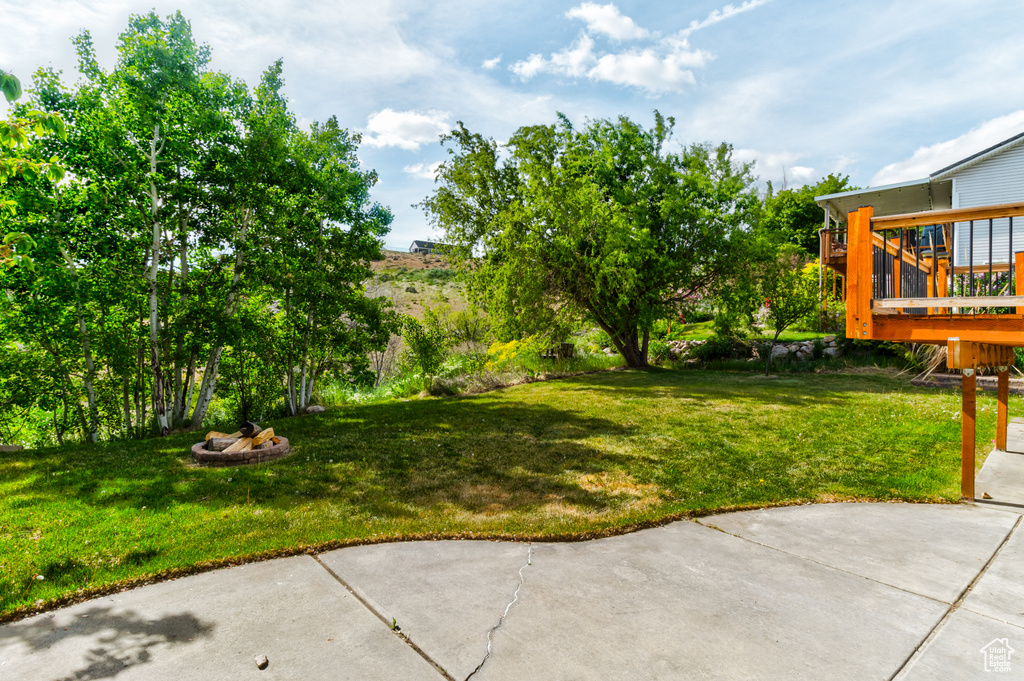 View of grassy yard featuring a wooden deck, a patio area, and an outdoor fire pit
