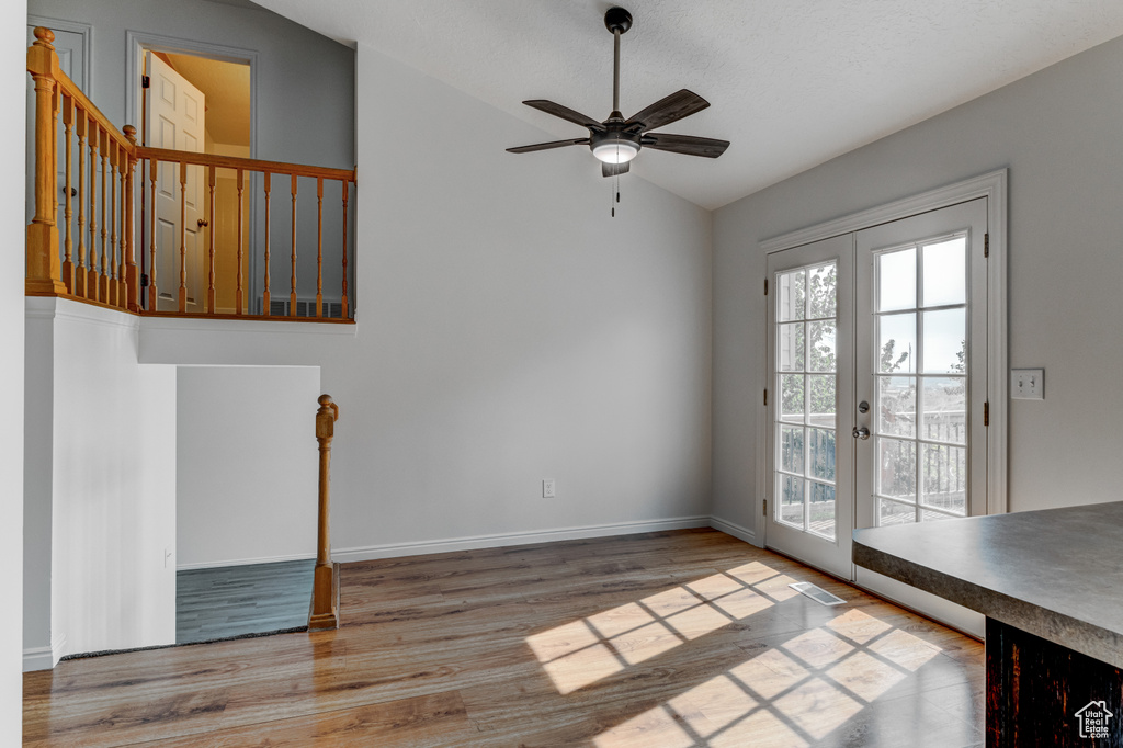 Unfurnished dining area with french doors, a ceiling fan, wood finished floors, lofted ceiling, and baseboards