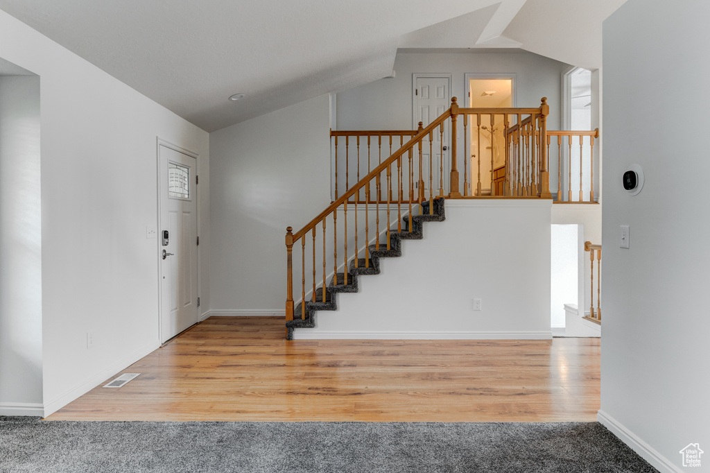 Entryway featuring vaulted ceiling, wood finished floors, stairs, and baseboards