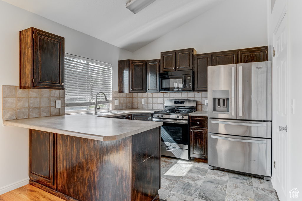 Kitchen with appliances with stainless steel finishes, a sink, lofted ceiling, a peninsula, and light countertops