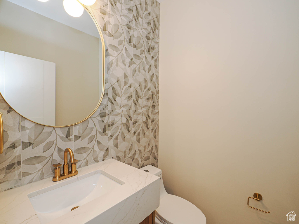 Bathroom featuring toilet, wallpapered walls, and vanity