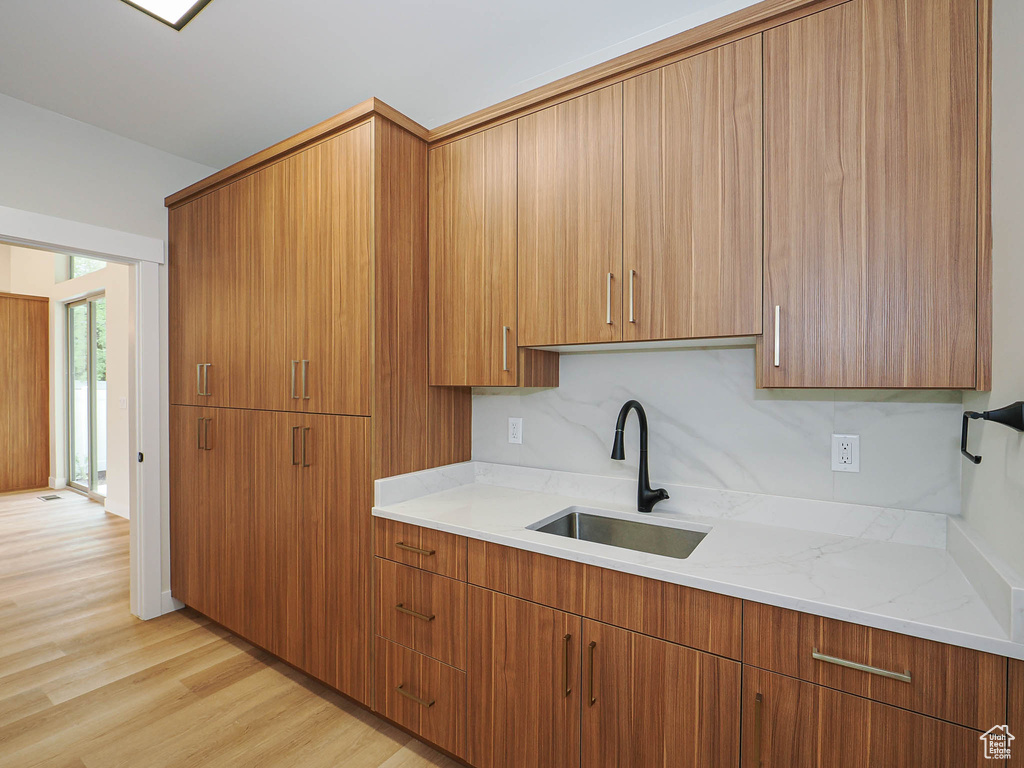 Kitchen featuring a sink, light wood finished floors, light stone counters, and brown cabinetry