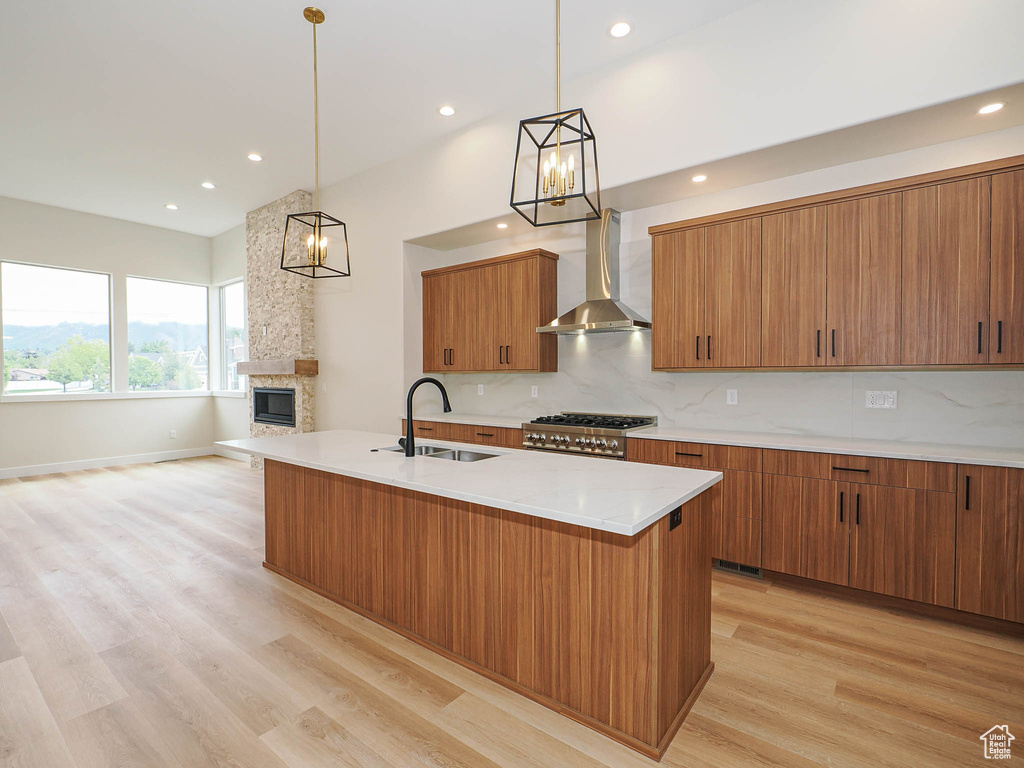 Kitchen with a sink, wall chimney range hood, a chandelier, light wood-style flooring, and brown cabinets