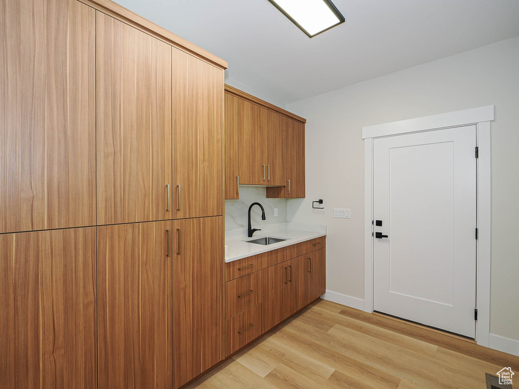 Laundry area featuring a sink, light wood-style flooring, and baseboards