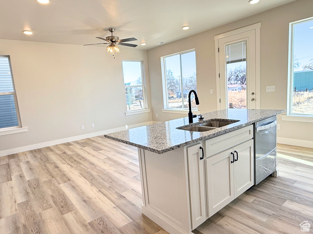 Kitchen with a sink, dishwasher, light wood finished floors, a center island with sink, and recessed lighting