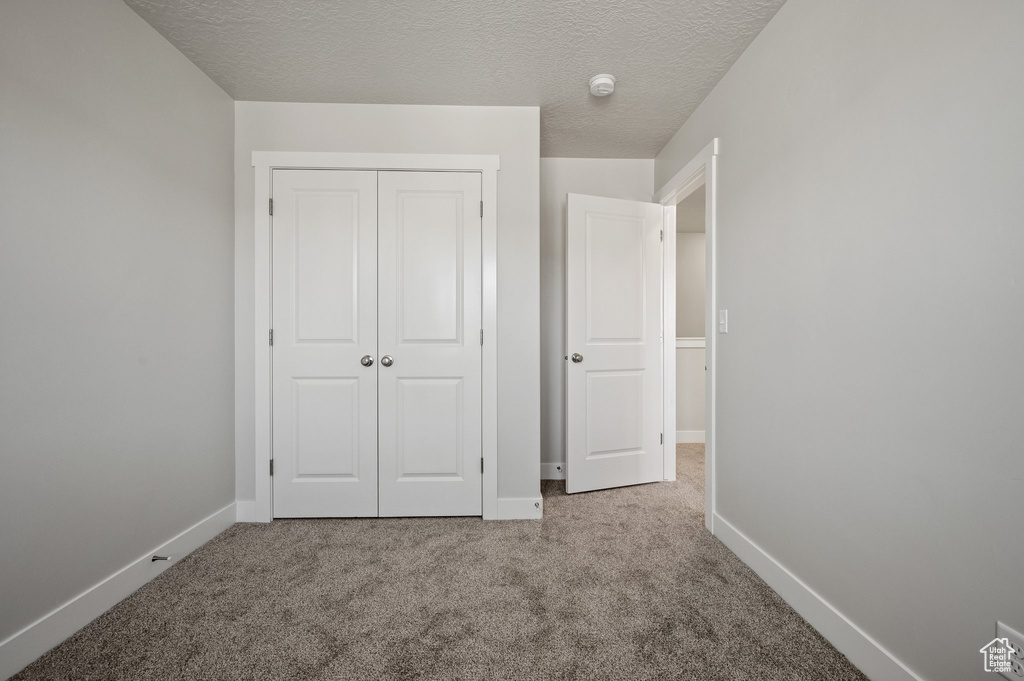 Unfurnished bedroom featuring carpet, a closet, baseboards, and a textured ceiling