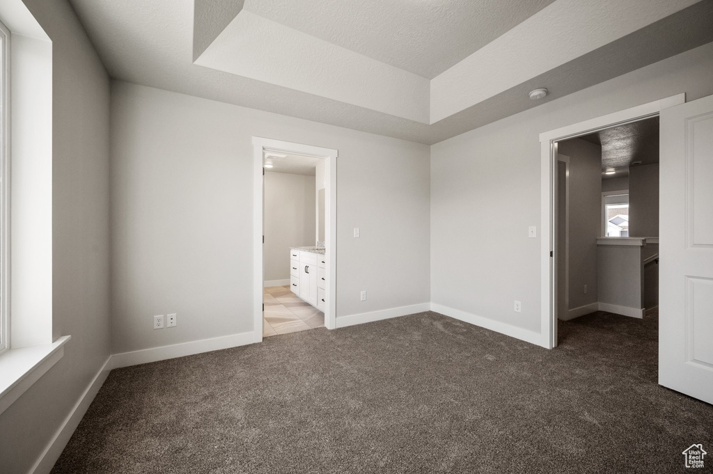 Unfurnished bedroom featuring carpet floors, baseboards, ensuite bathroom, and a tray ceiling
