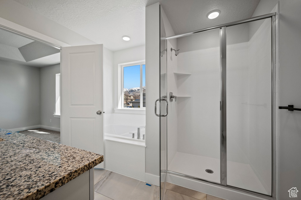 Full bath with a stall shower, a bath, a textured ceiling, and baseboards