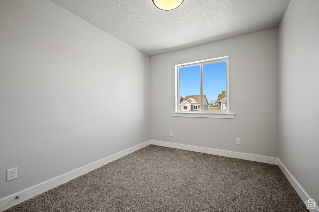 Empty room with a textured ceiling, dark carpet, and baseboards