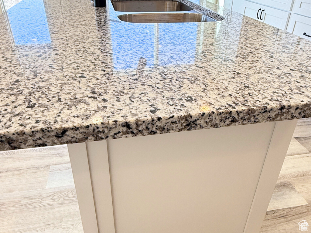 Kitchen view of light stone counters, wood finished floors, and a sink