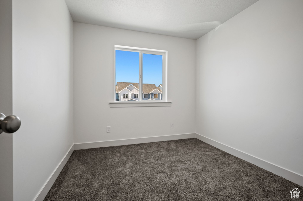 Spare room featuring dark colored carpet and baseboards