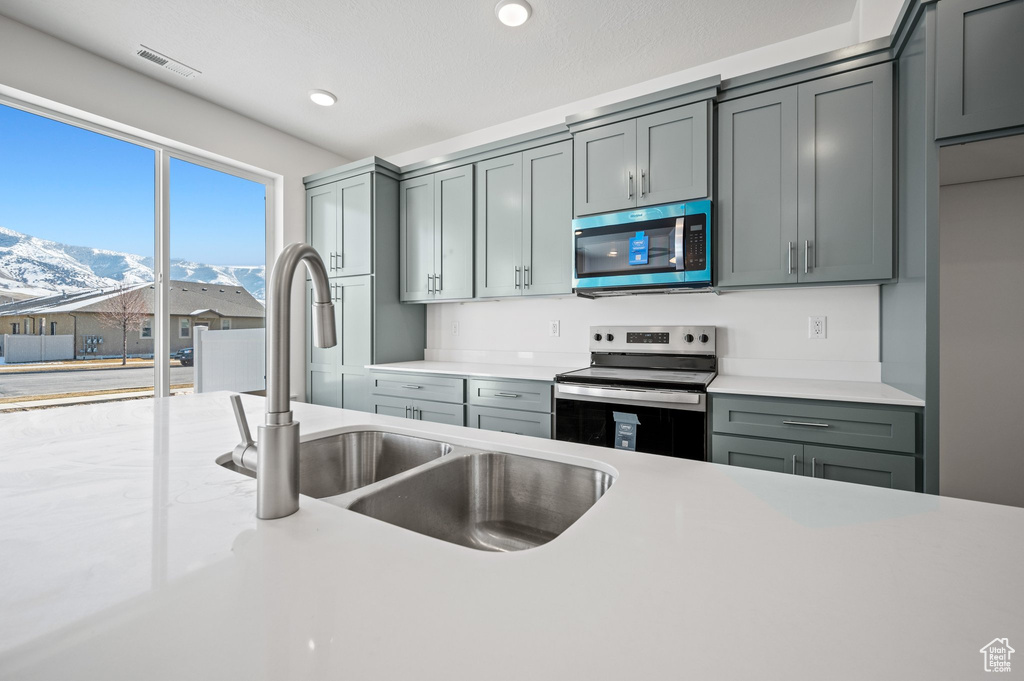 Kitchen featuring stainless steel appliances, a sink, a mountain view, light countertops, and gray cabinetry