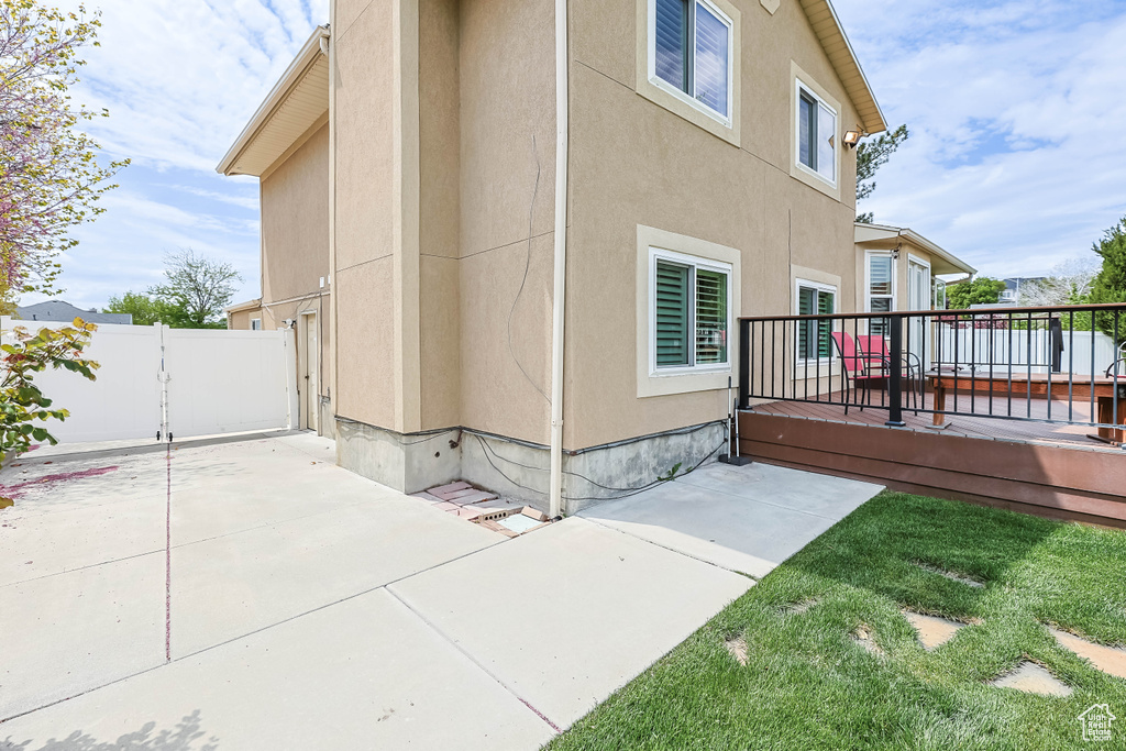 View of side of home with a patio area, stucco siding, a wooden deck, and fence