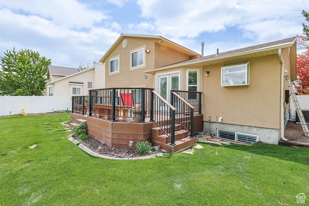 Back of house featuring stucco siding, a deck, a lawn, and fence private yard