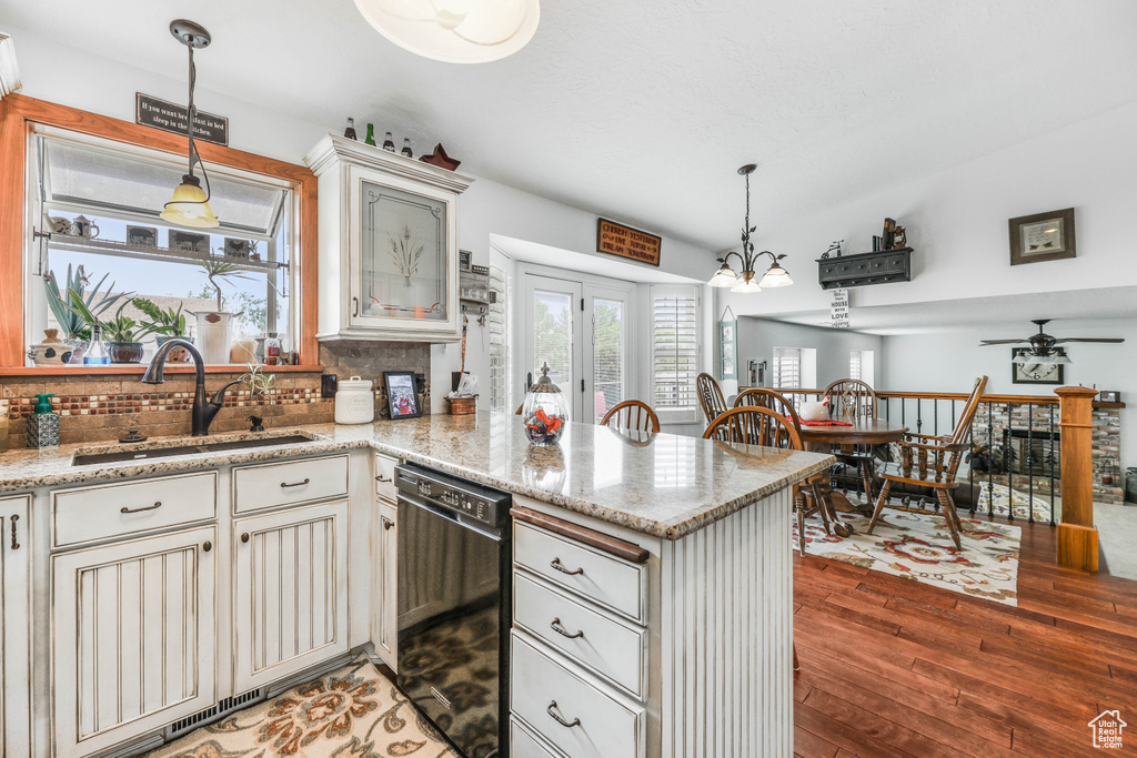 Kitchen featuring a peninsula, wood finished floors, a sink, backsplash, and dishwasher