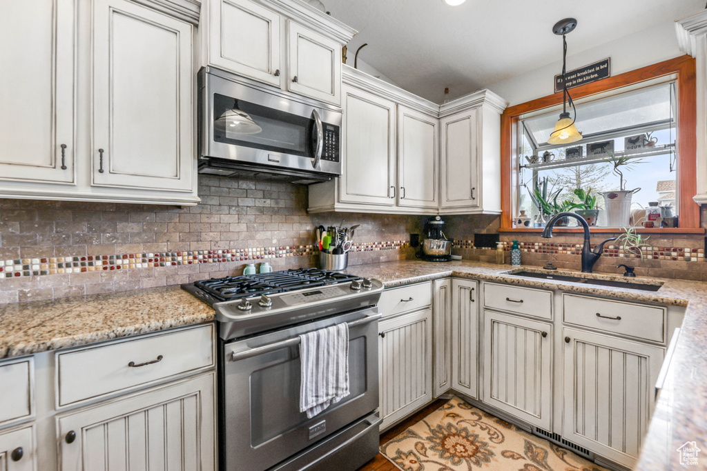 Kitchen featuring a sink, tasteful backsplash, decorative light fixtures, light stone countertops, and appliances with stainless steel finishes