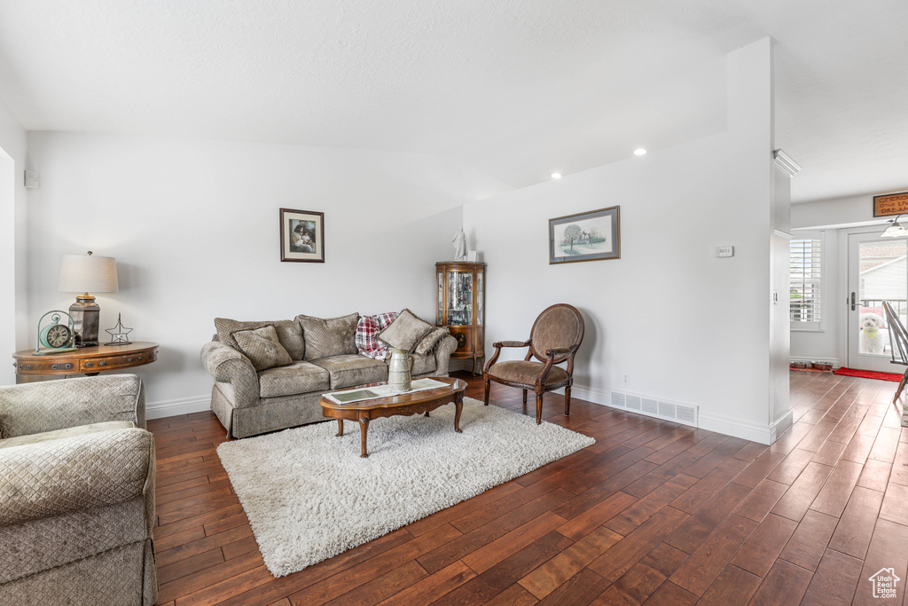 Living room with vaulted ceiling, visible vents, baseboards, and dark wood-style floors