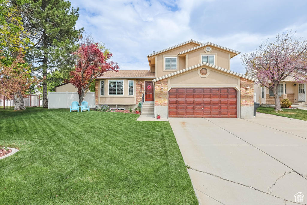 Tri-level home featuring stucco siding, fence, a front yard, brick siding, and driveway