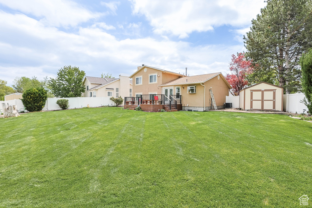 Back of house with a storage shed, stucco siding, a wooden deck, a fenced backyard, and an outbuilding