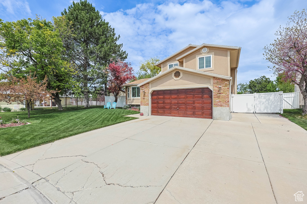 View of front facade featuring driveway, a front lawn, fence, and a gate