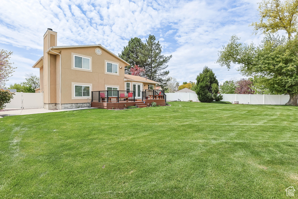 Rear view of property with stucco siding, a chimney, a lawn, a wooden deck, and a fenced backyard