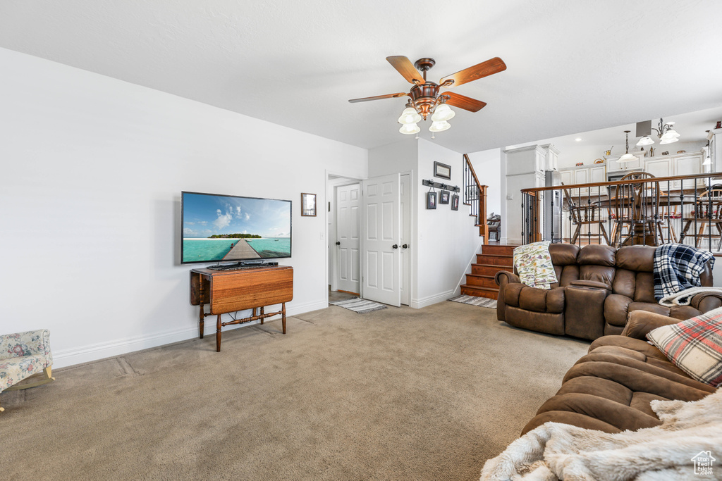 Living area featuring carpet flooring, baseboards, ceiling fan, and stairs