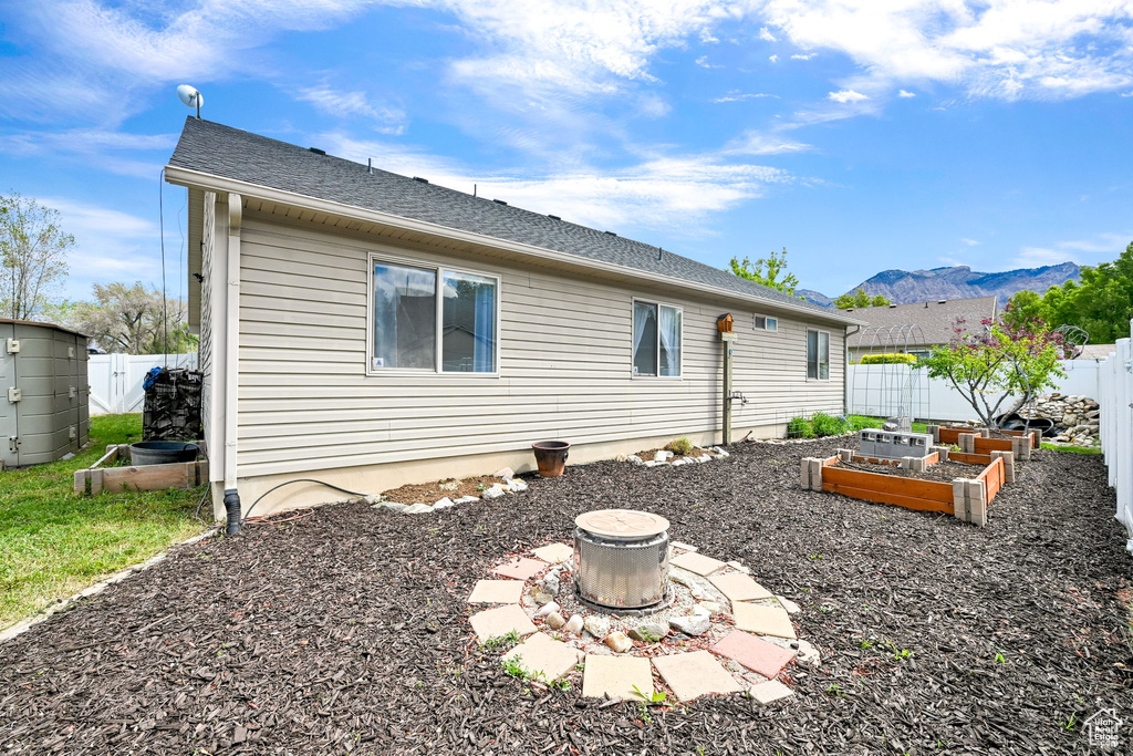 Back of property featuring a vegetable garden, a fenced backyard, a mountain view, and a shingled roof