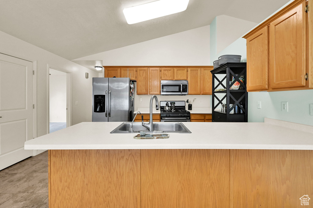 Kitchen with appliances with stainless steel finishes, a sink, vaulted ceiling, light countertops, and a peninsula