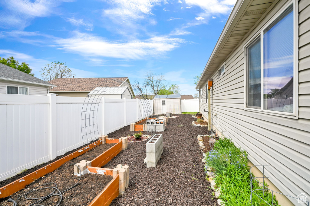 Fenced backyard featuring a vegetable garden, an outdoor structure, and a storage unit