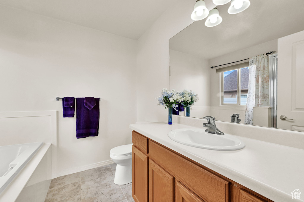 Full bath featuring a chandelier, vanity, toilet, a garden tub, and baseboards