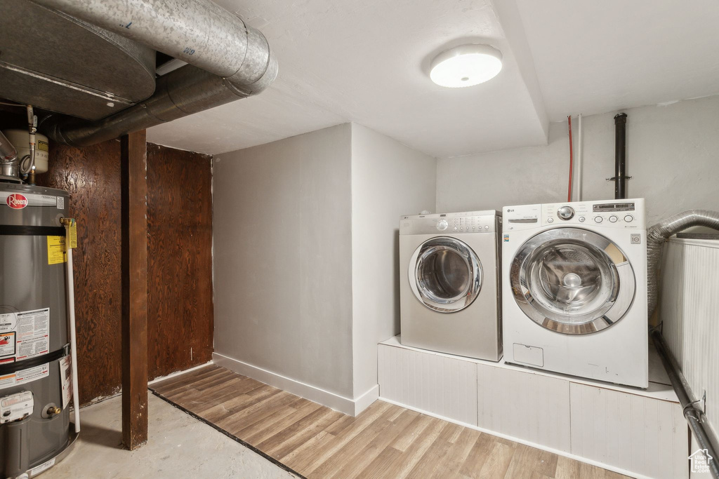 Laundry room featuring baseboards, strapped water heater, wood finished floors, washing machine and clothes dryer, and laundry area