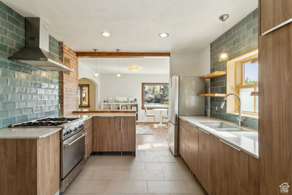 Kitchen featuring a sink, a peninsula, open shelves, wall chimney exhaust hood, and appliances with stainless steel finishes